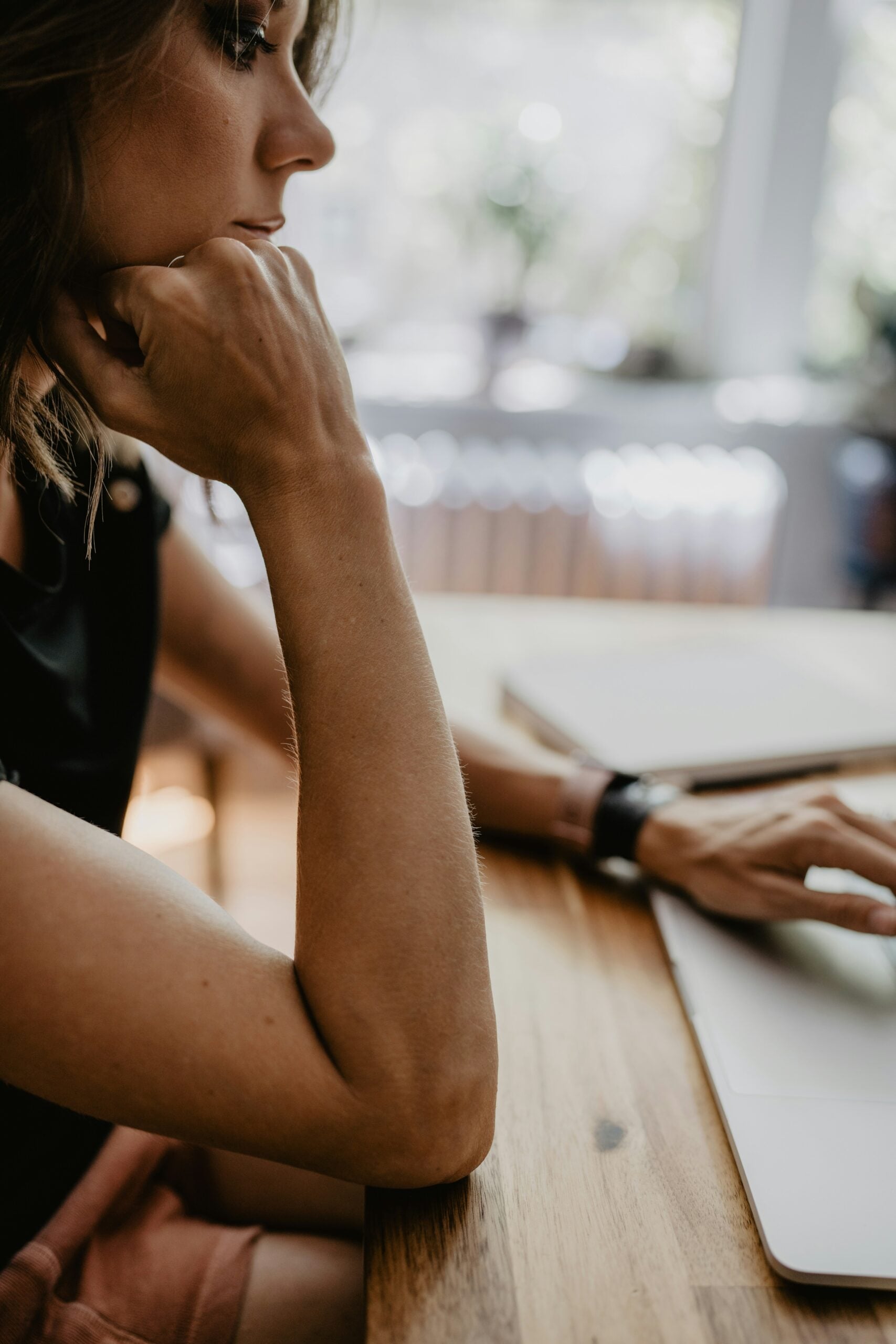 Woman reviewing her finances while working on a laptop at a wooden desk.
