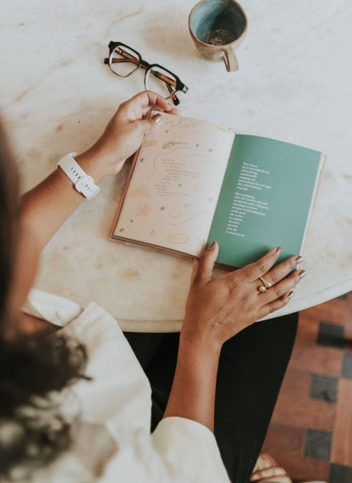 Person reading a poetry book at a table with a cup of coffee, illustrating a mindful reading practice for relaxation and self-reflection.