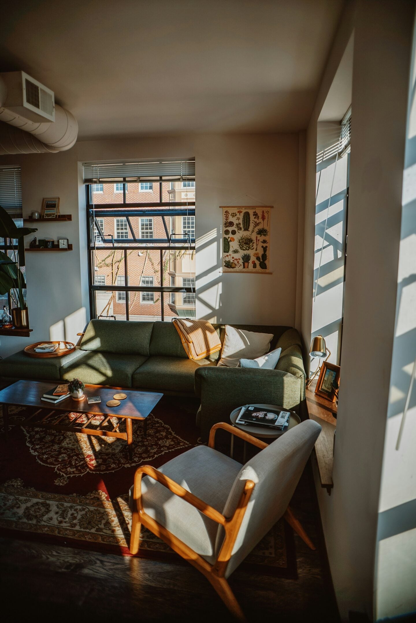 Cozy small living room with a green sofa, wooden coffee table, accent chair, large windows, and warm natural sunlight creating an open, airy feel.
