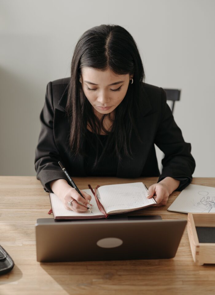 Business owner reviewing notes and planning growth strategy while working at a laptop in a home office.