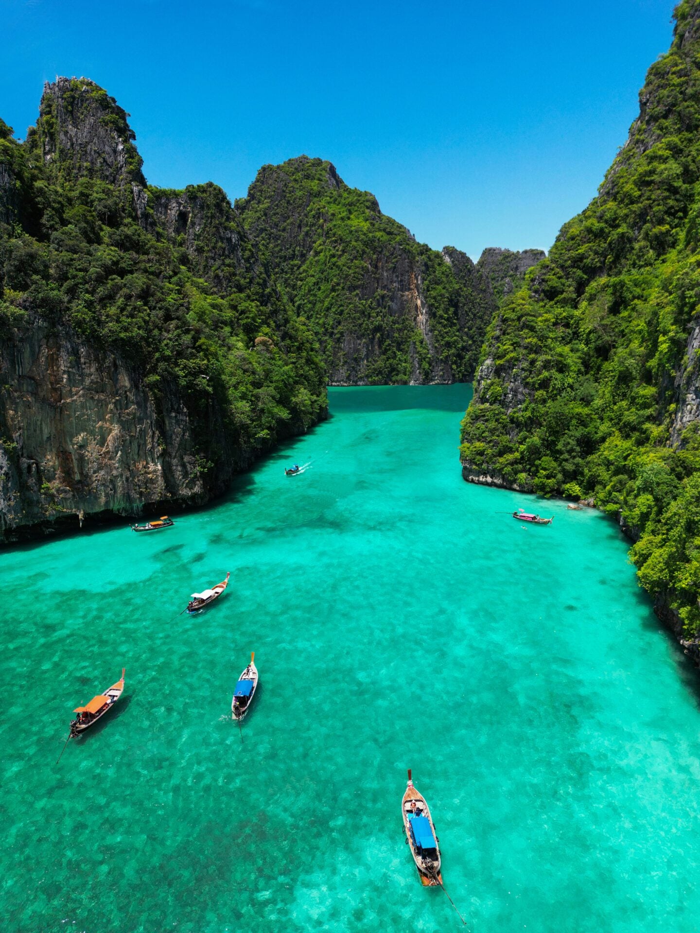 Long-tail boats floating on the turquoise waters of Pi Leh Lagoon surrounded by limestone cliffs in Krabi, Thailand.