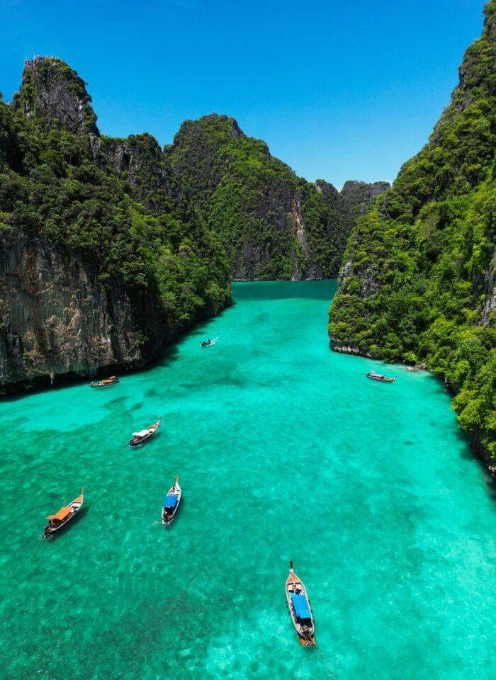Long-tail boats floating on the turquoise waters of Pi Leh Lagoon surrounded by limestone cliffs in Krabi, Thailand.