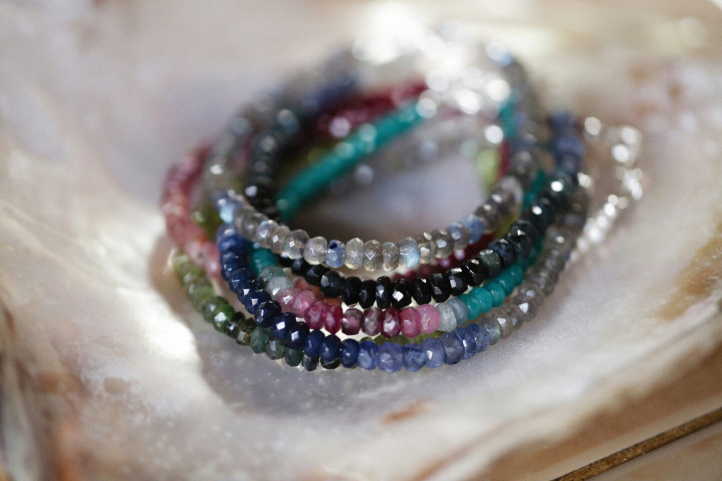 Stack of colorful handmade gemstone beaded bracelets displayed on a polished stone tray.