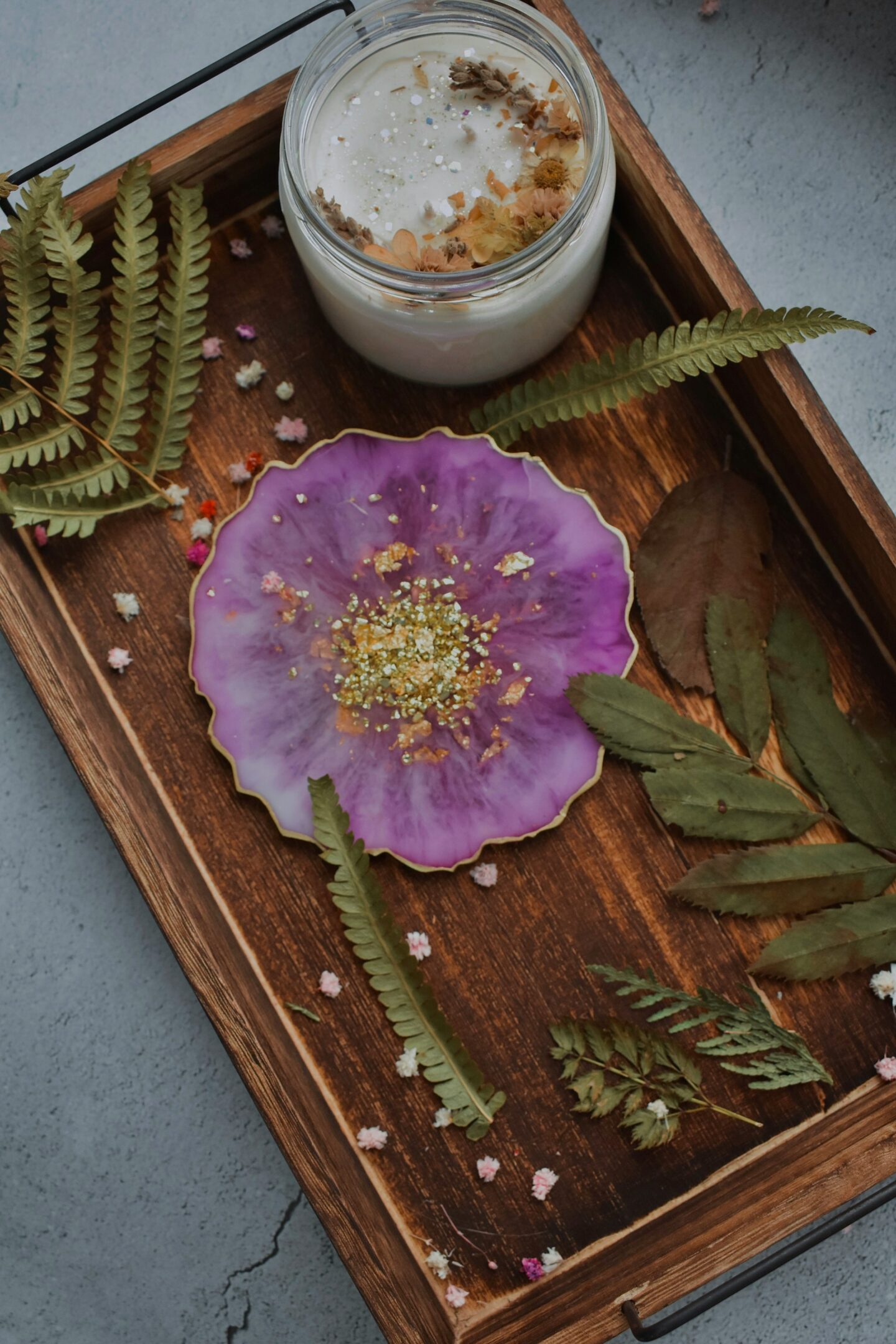 Handmade purple resin coaster with gold edging displayed on a wooden tray beside a scented candle and dried greenery.