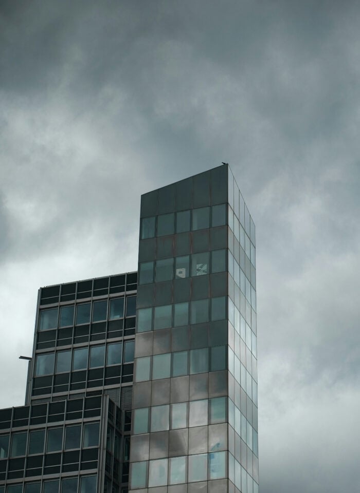 Modern glass office buildings beneath dark, stormy clouds, symbolizing the growing impact of severe weather on business operations, insurance risk, and commercial property exposure.