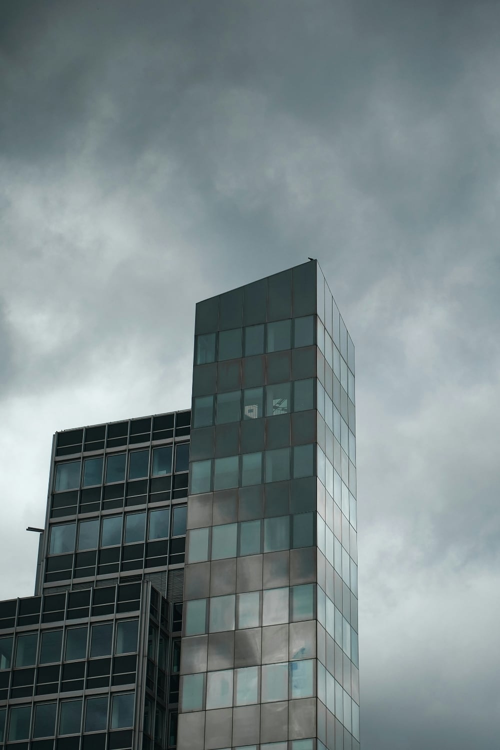 Modern glass office buildings beneath dark, stormy clouds, symbolizing the growing impact of severe weather on business operations, insurance risk, and commercial property exposure.