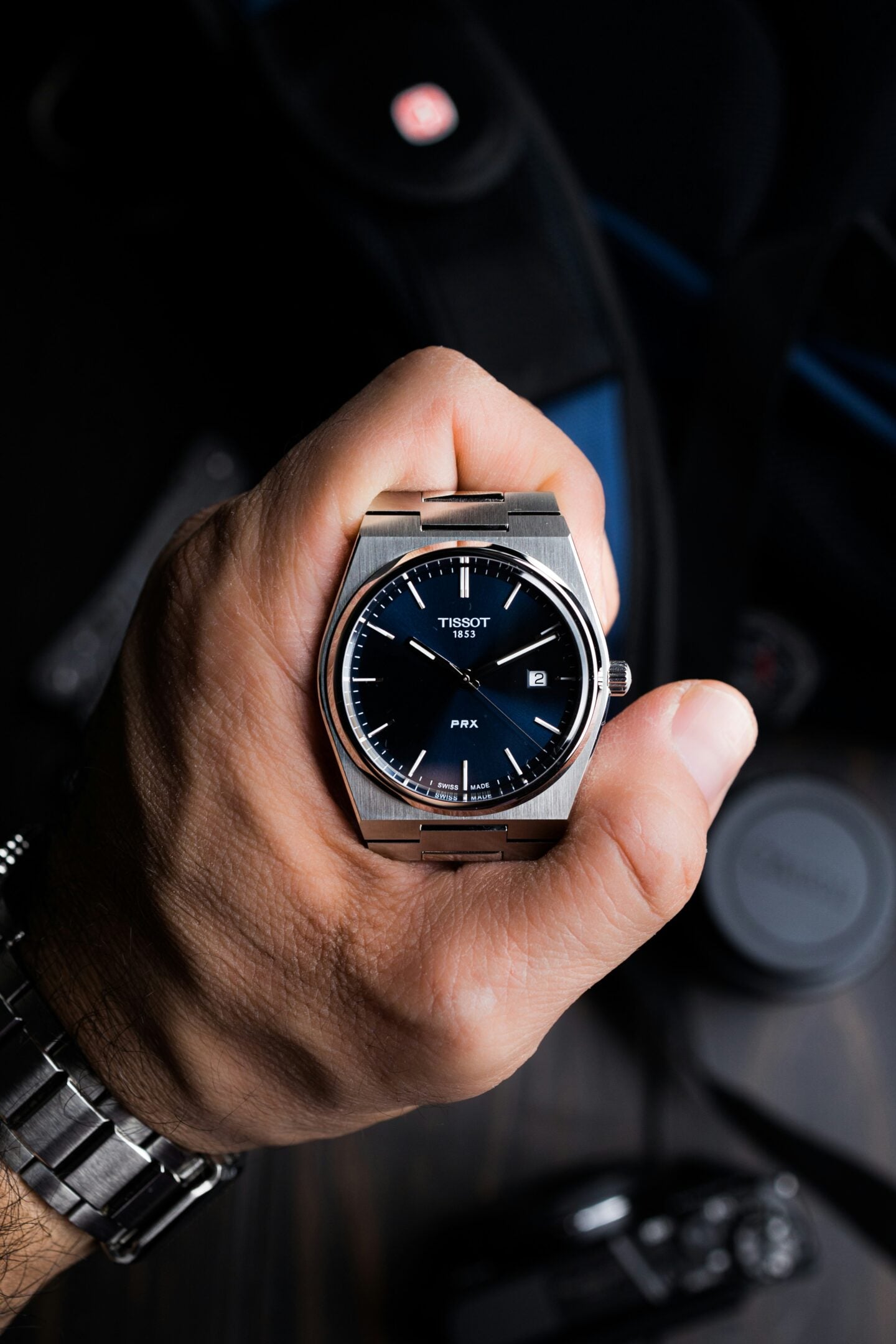 Close-up of a hand holding a silver Tissot PRX watch with a blue dial and stainless steel bracelet.