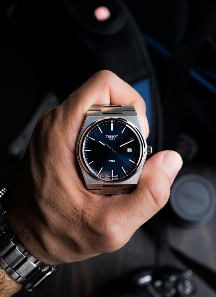 Close-up of a hand holding a silver Tissot PRX watch with a blue dial and stainless steel bracelet.