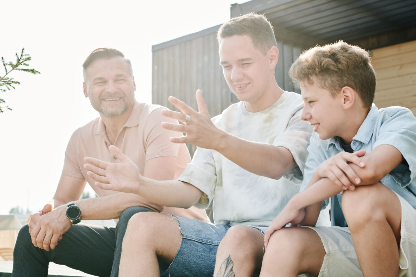Father sitting outdoors and talking with two teenage sons about preparing for adulthood and independence.
