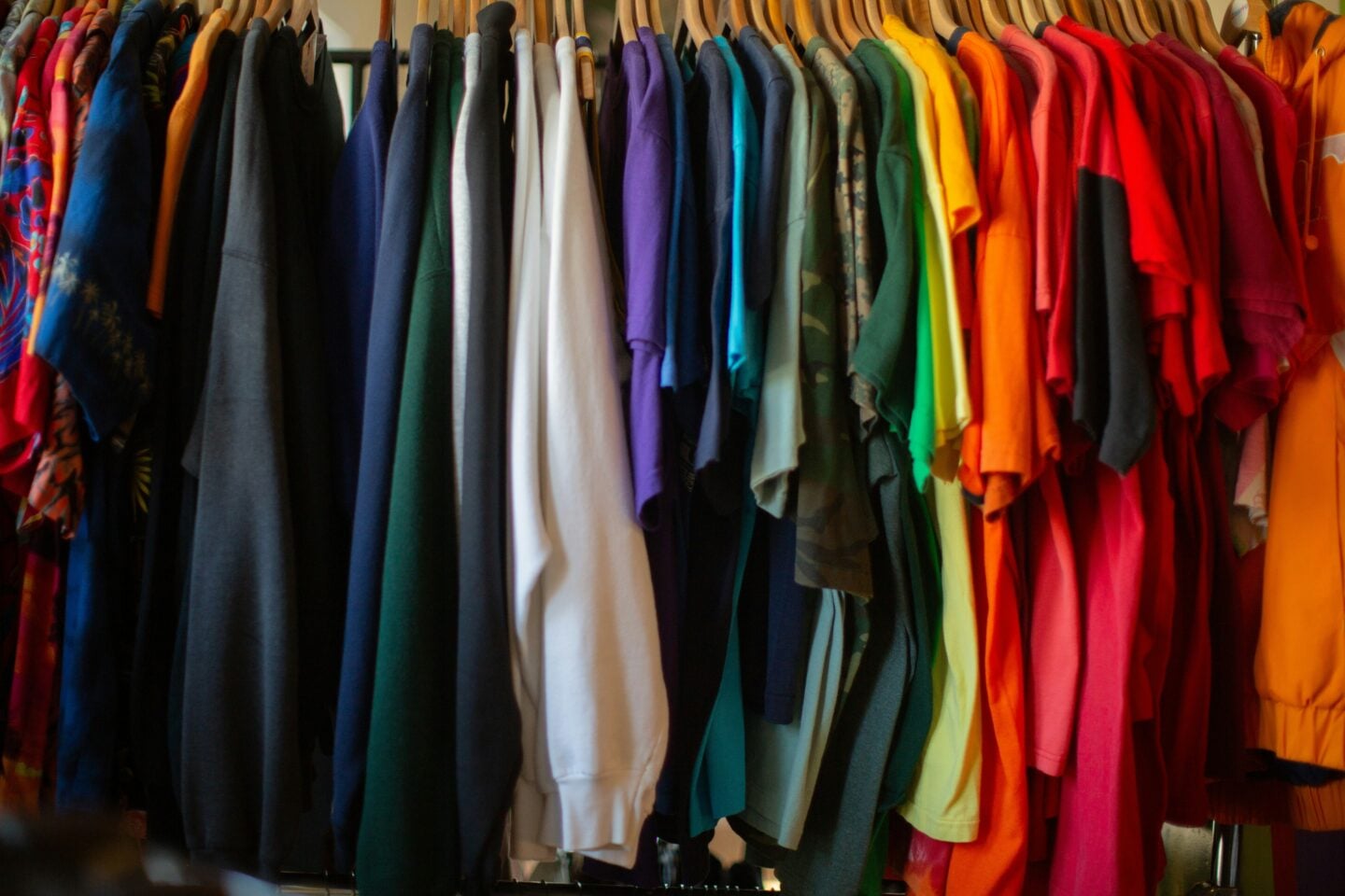 Colorful clothes in a range of bright and neutral shades hanging on a wardrobe rail.