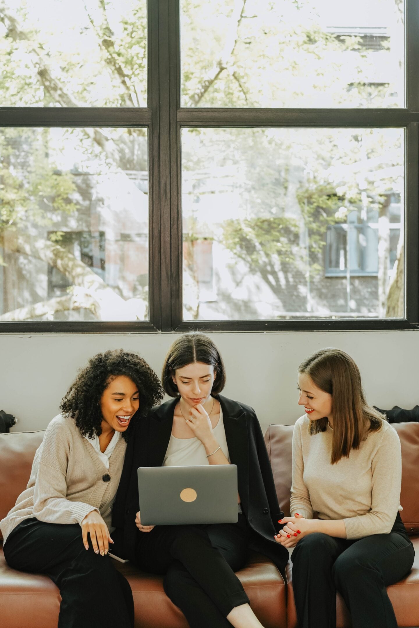 Three women sitting on a sofa looking at a laptop together.