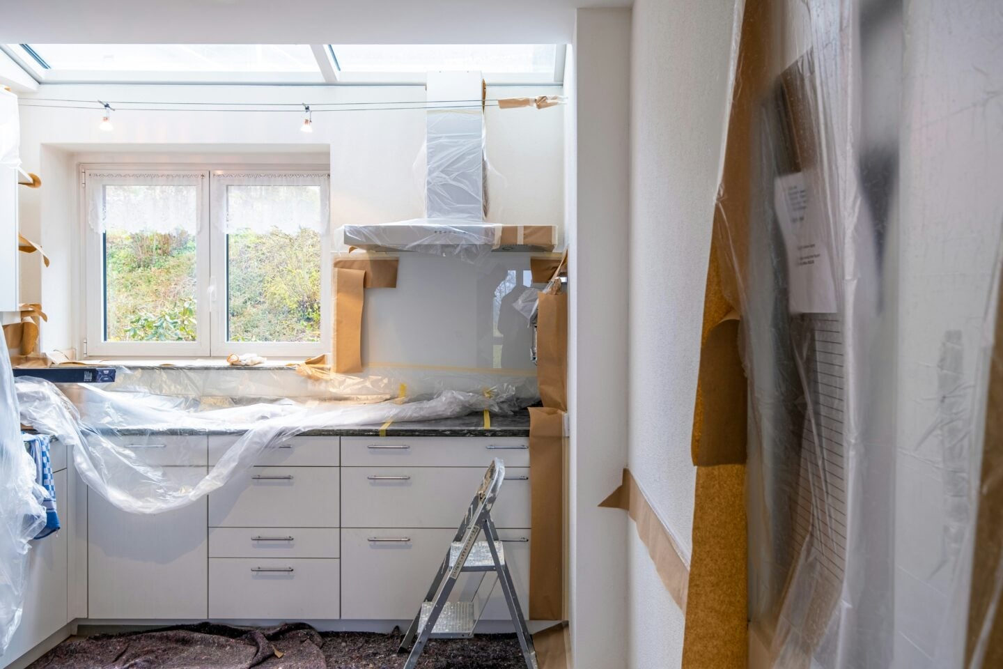 Modern kitchen undergoing renovation with cabinets and countertops protected by plastic sheeting, illustrating a home improvement project in progress.