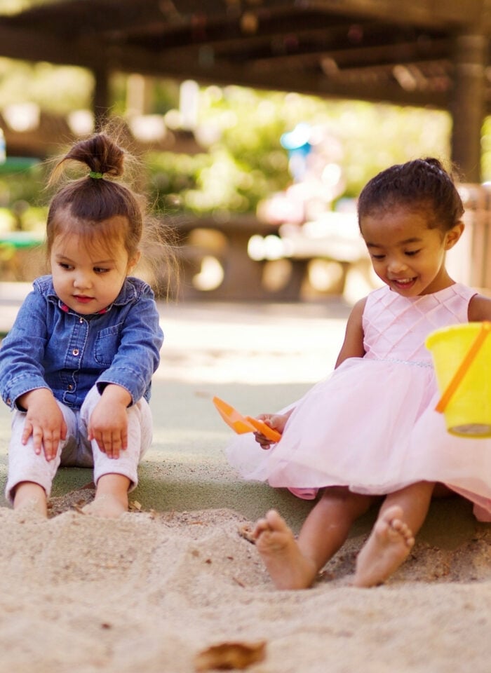 Three young children playing together in a sandbox at an outdoor playground.