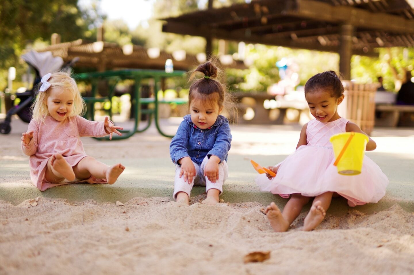 Three young children playing together in a sandbox at an outdoor playground.