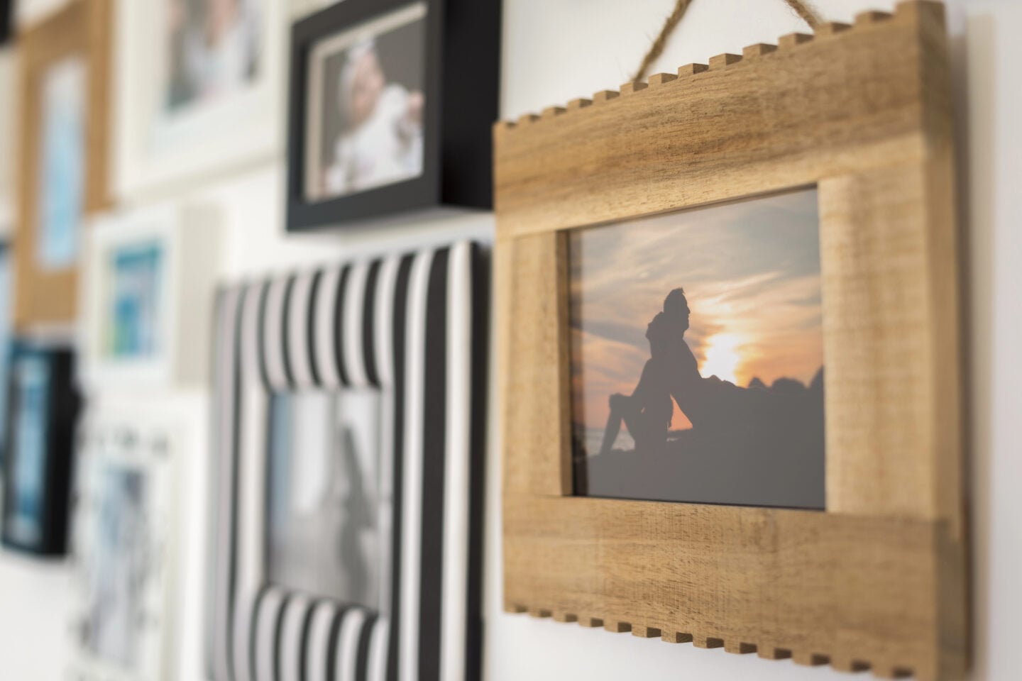 Collection of framed personal photographs displayed together on a wall, including a sunset photo in a wooden frame.