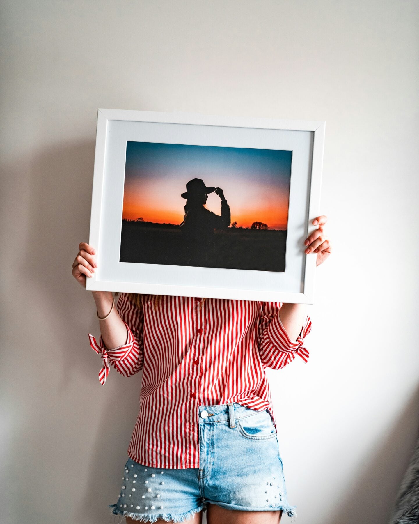 Person holding a large framed sunset photograph ready to display at home.