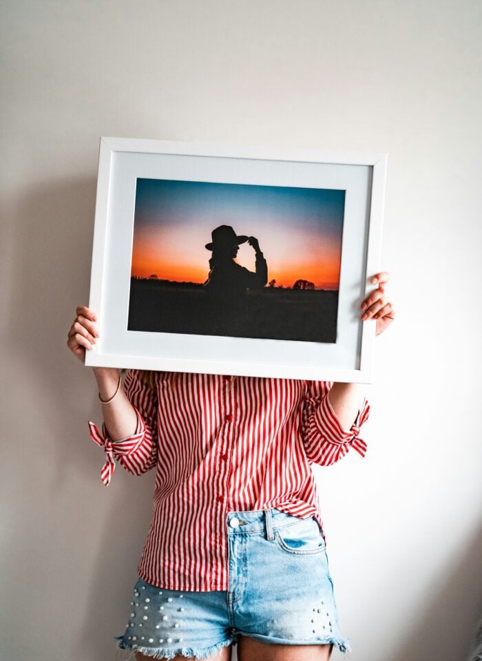 Person holding a large framed sunset photograph ready to display at home.