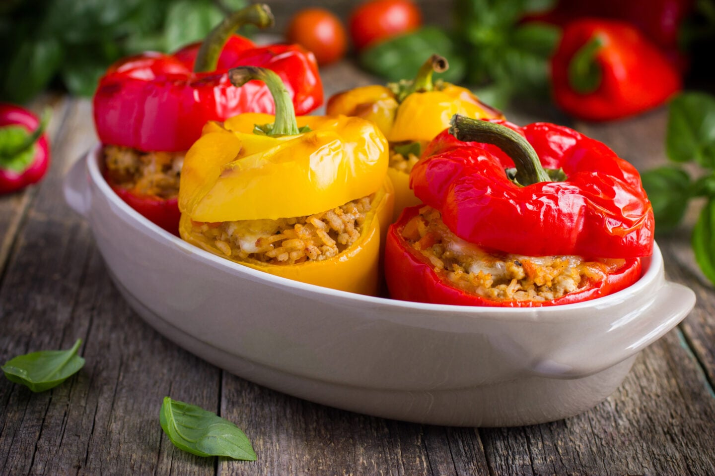 Red and yellow bell peppers stuffed with rice and vegetables in a baking dish.