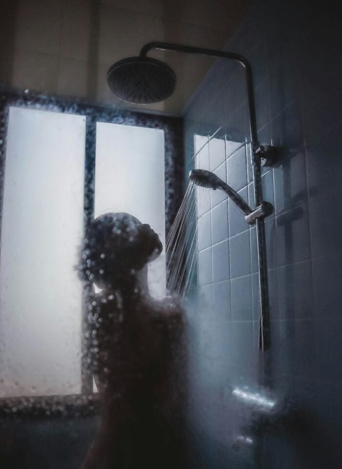 Woman washing her hair under a handheld shower head in a steamy bathroom.