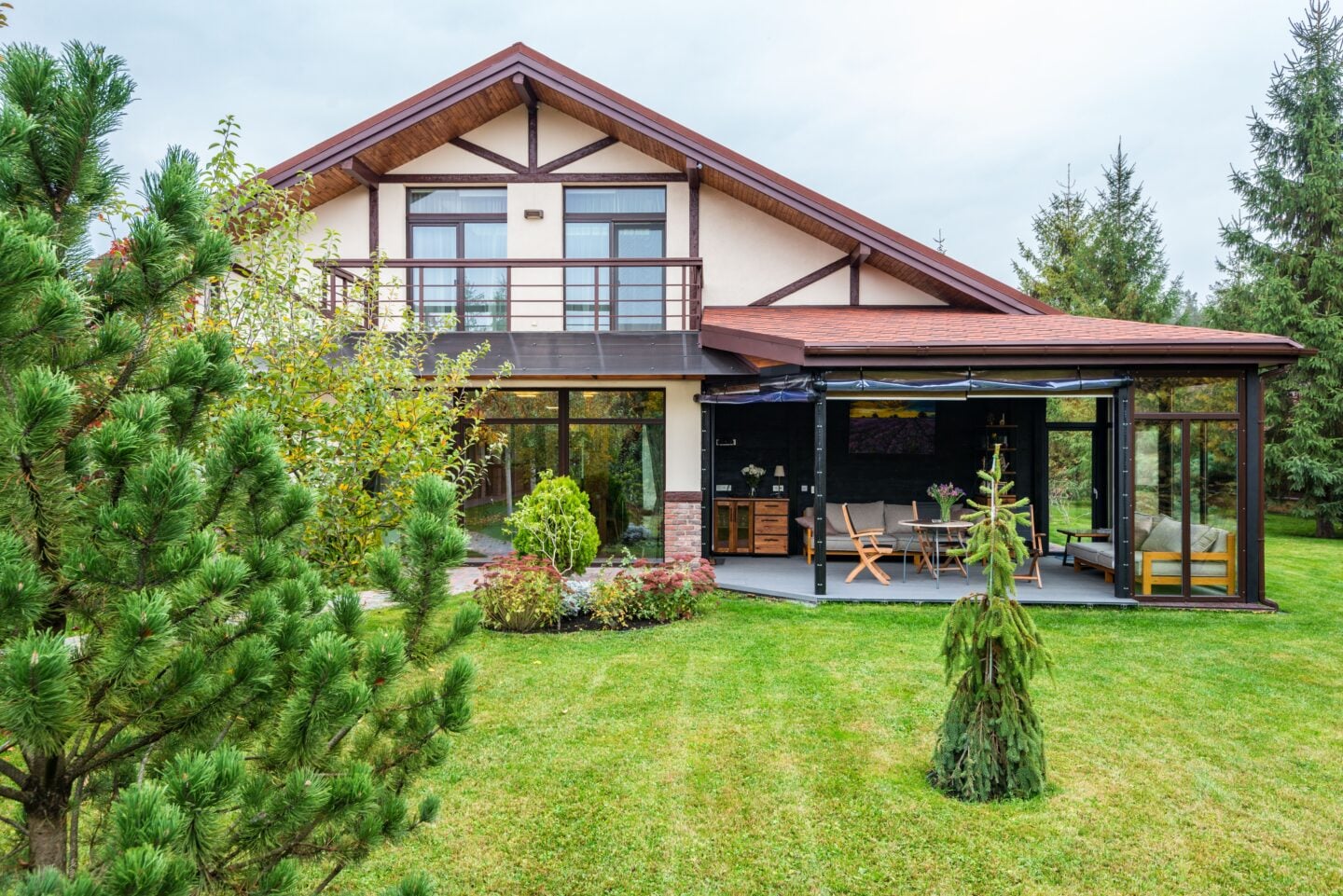 Modern two storey house with a covered outdoor living area, patio furniture and a large landscaped garden surrounded by trees.