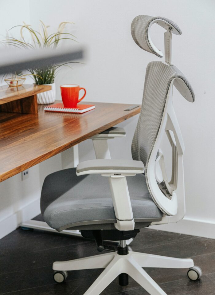Grey ergonomic office chair with adjustable headrest, armrests and lumbar support positioned beside a wooden home office desk.