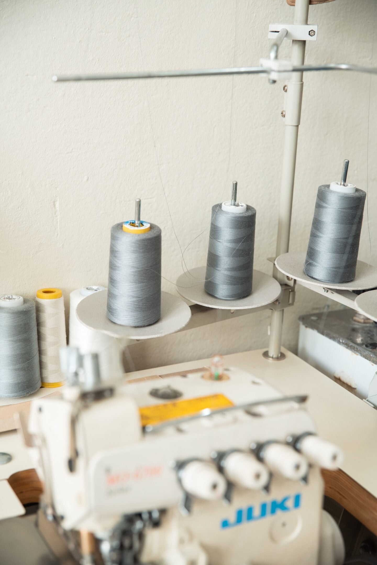 Industrial sewing machine with large grey and white thread spools in a sewing workspace.