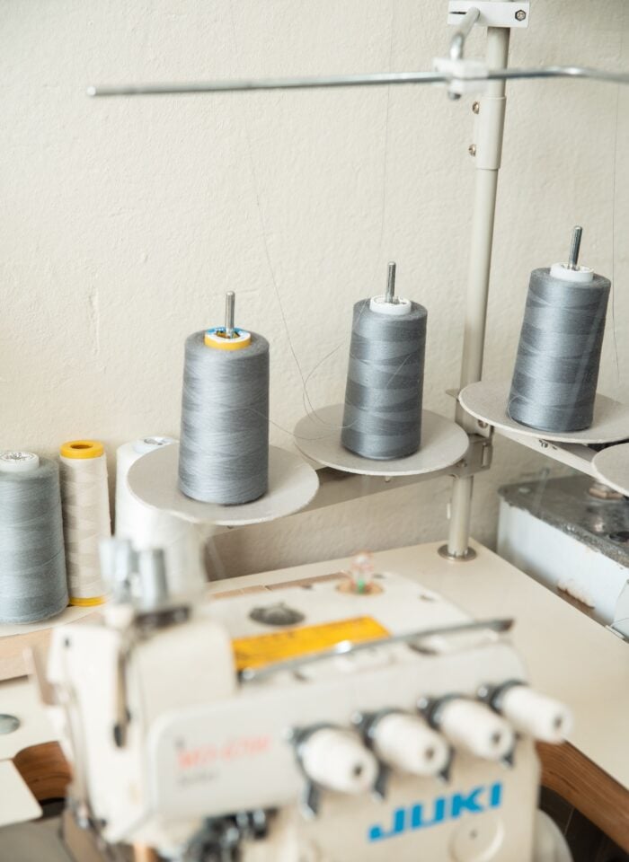 Industrial sewing machine with large grey and white thread spools in a sewing workspace.
