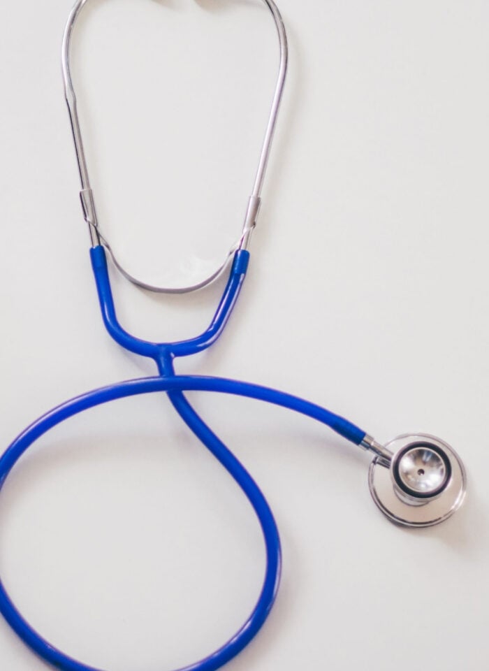Blue stethoscope beside a laptop on a white desk, representing healthcare and clinical business management.
