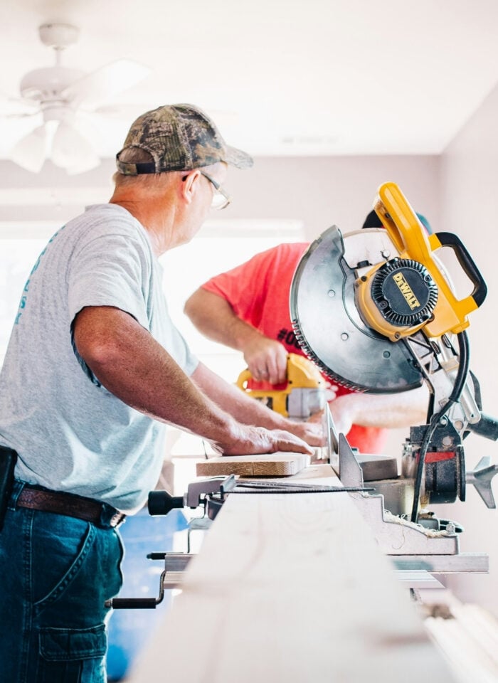 Two workers using a miter saw during a home renovation project.