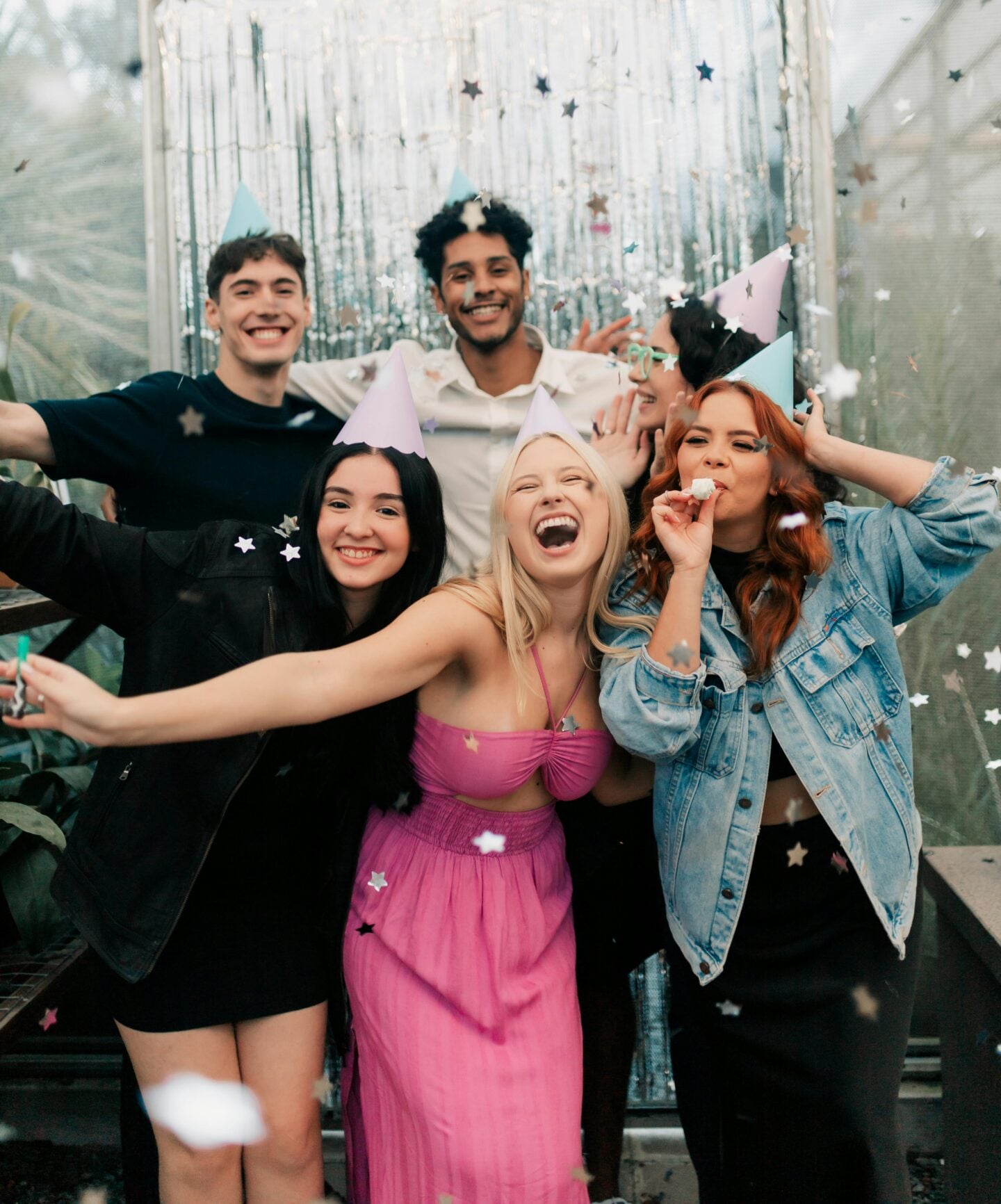 Group of friends wearing party hats smiling and posing together with confetti falling.