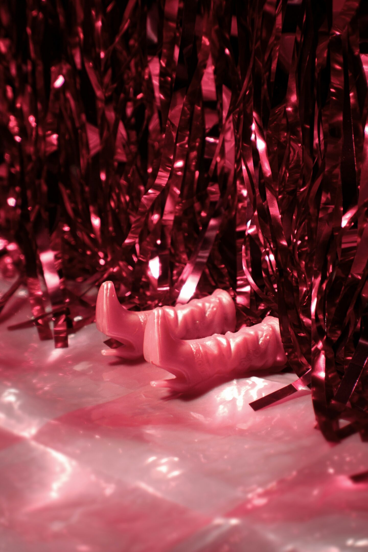 Pink tinsel curtain backdrop with small toy boots on a shiny surface.