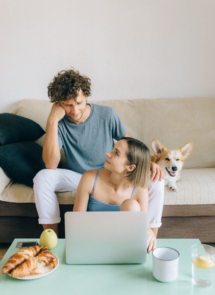 Couple reviewing their finances together on a laptop at home with their dog beside them.