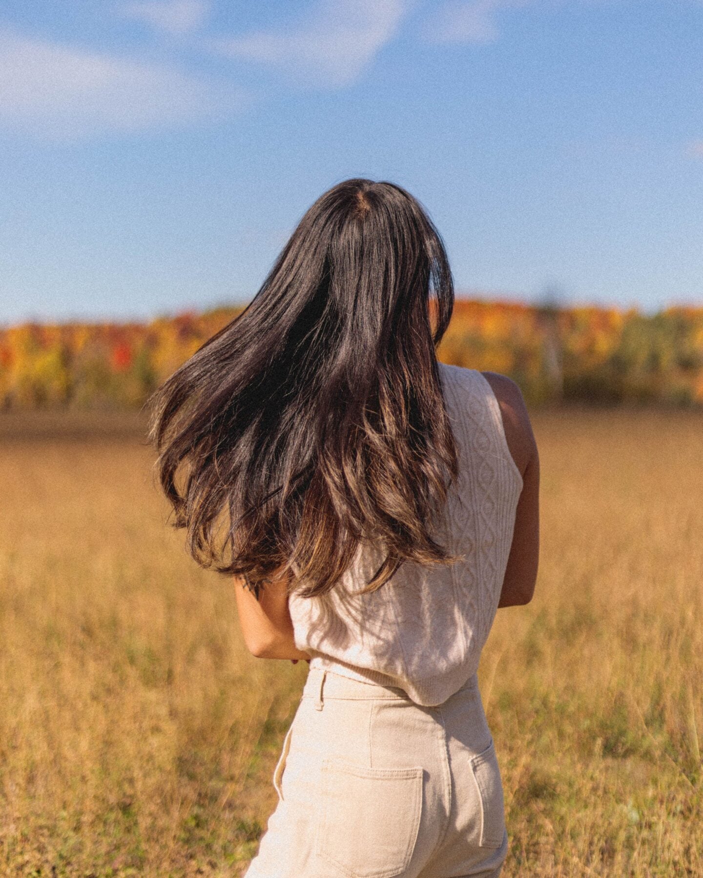 Woman wearing a cream sweater tank and neutral trousers in a sunlit autumn field.