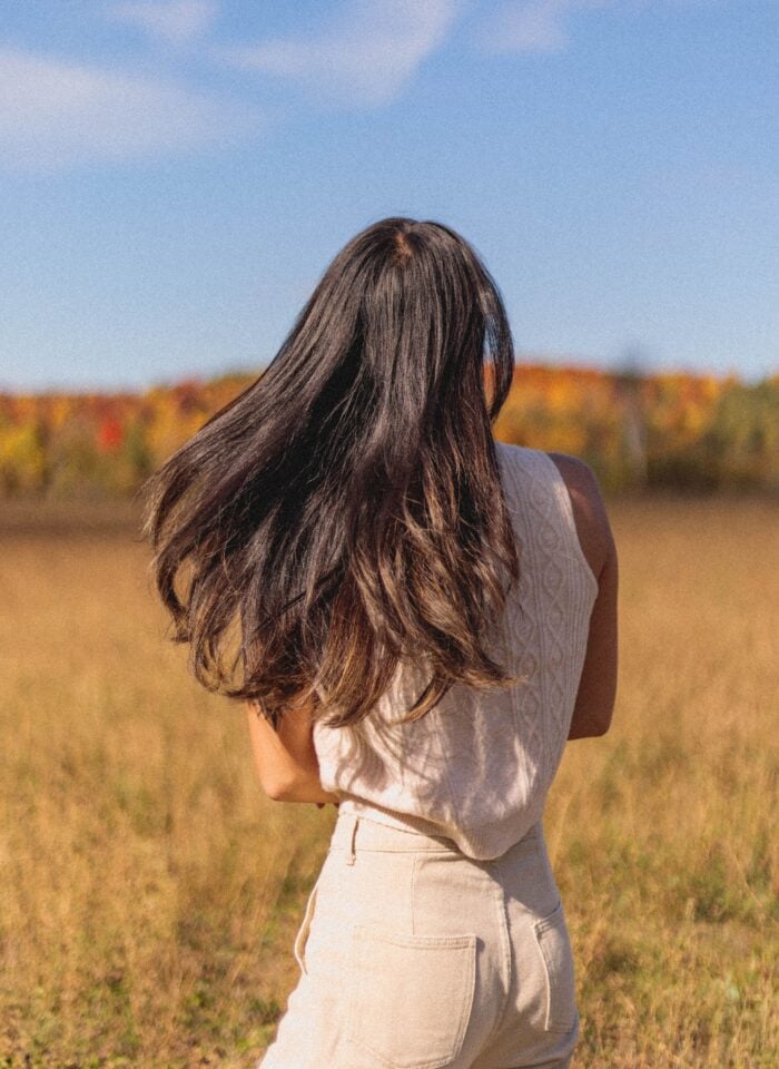 Woman wearing a cream sweater tank and neutral trousers in a sunlit autumn field.