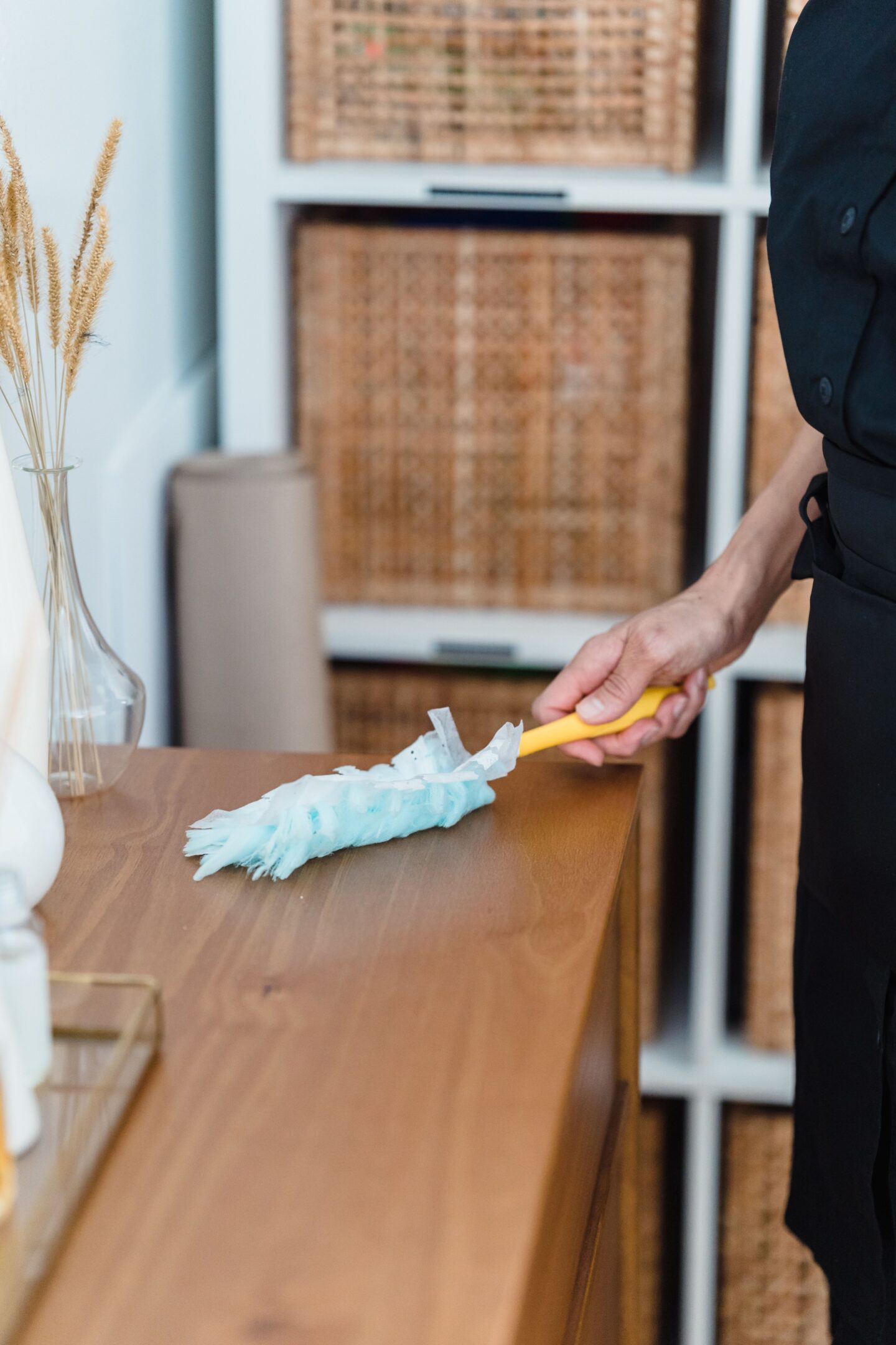 Person dusting a wooden cabinet with a feather duster in a bright, modern home.