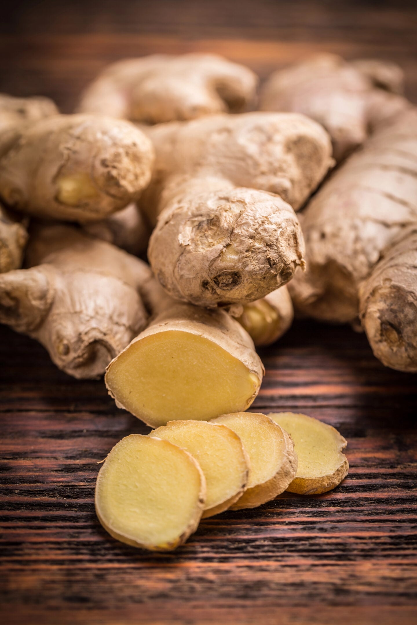 Fresh ginger root with sliced pieces arranged on a dark wooden surface.