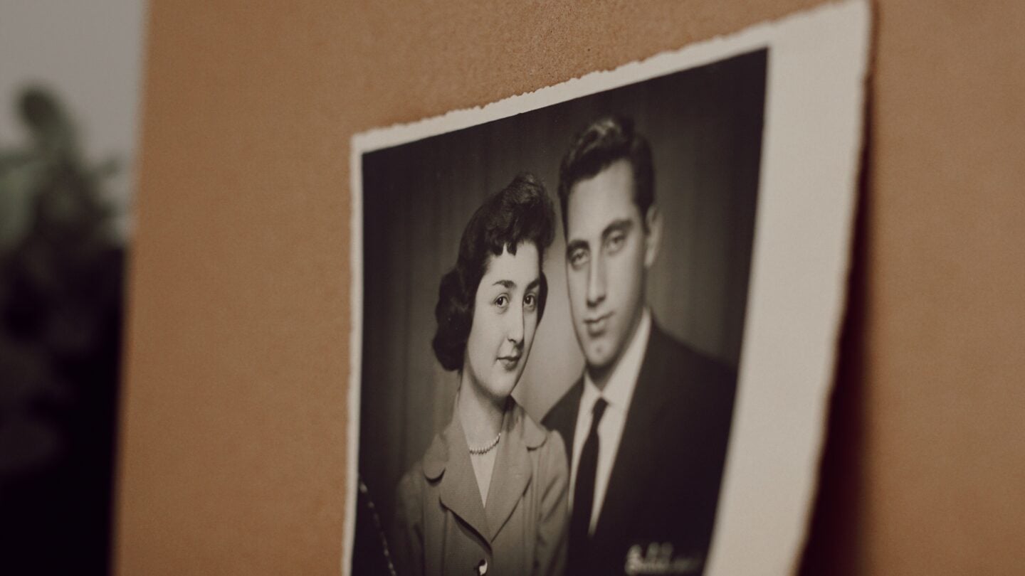 Vintage black-and-white printed photograph of a formally dressed couple, displayed against a warm brown background.