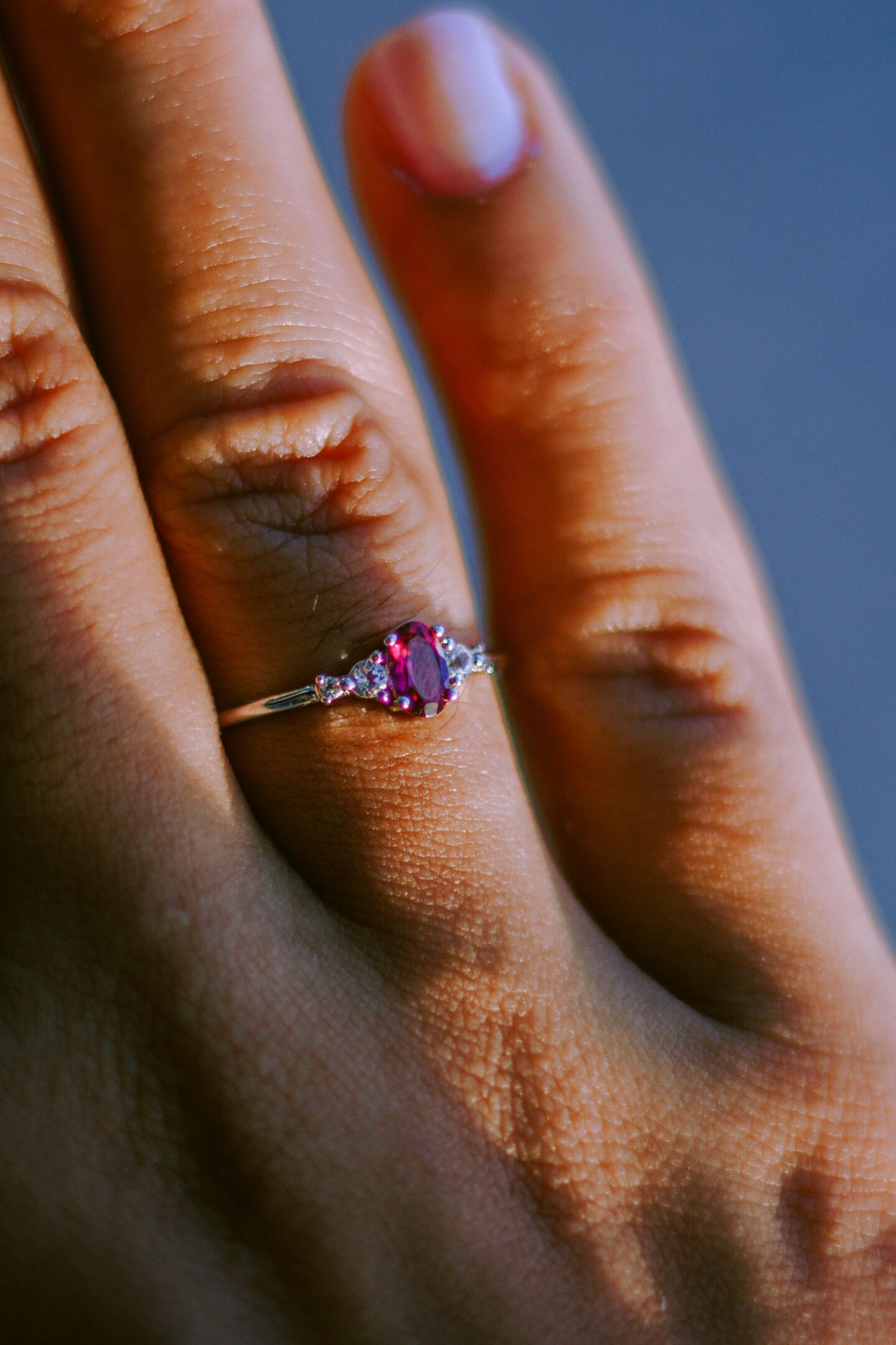 Ring with ruby: Close-up of a delicate silver ring featuring a vivid red ruby centre stone with small clear accent stones on a woman’s finger.
