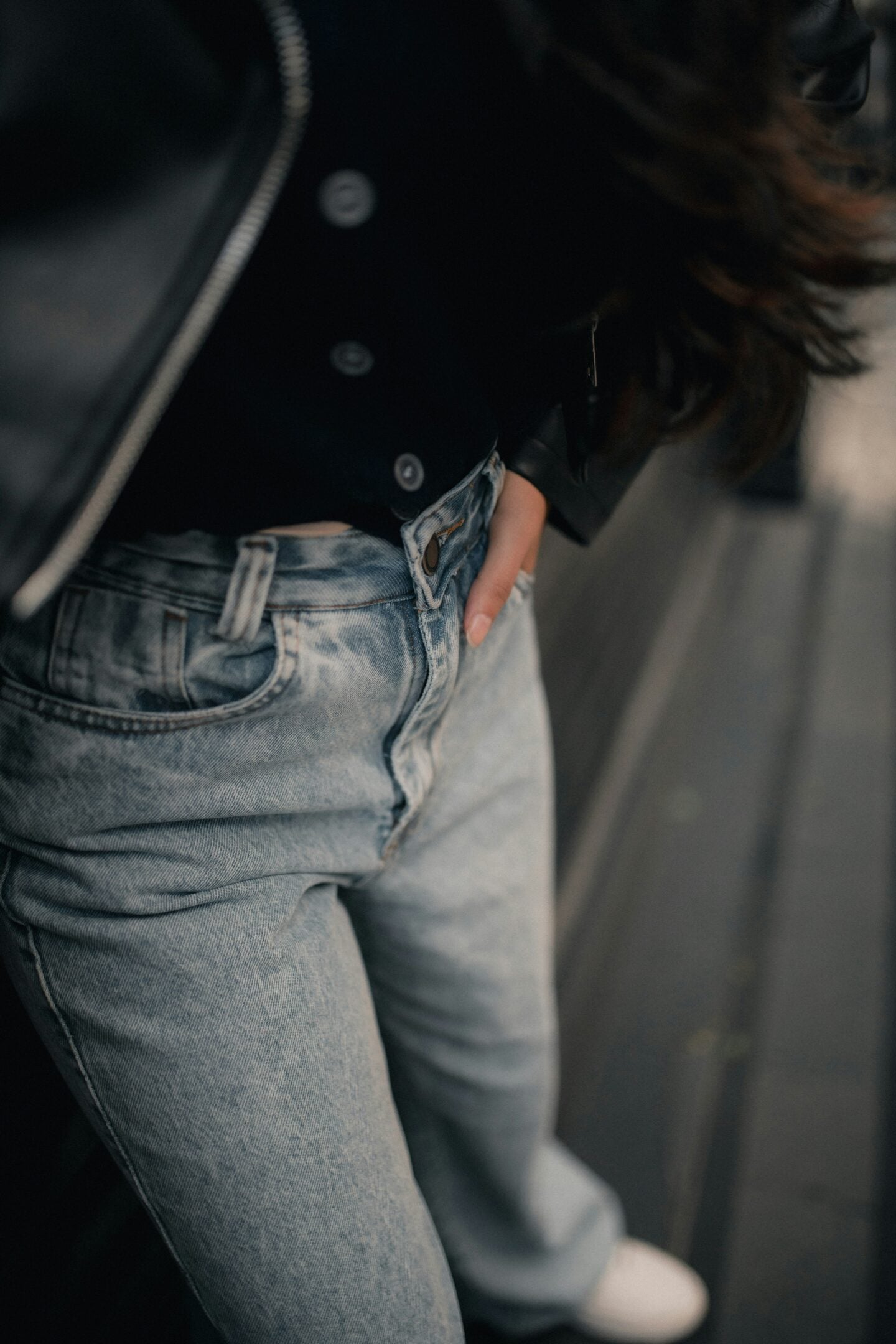 Close-up of a woman wearing well-fitted light-wash jeans with a black jacket, her hand tucked casually into the front pocket.