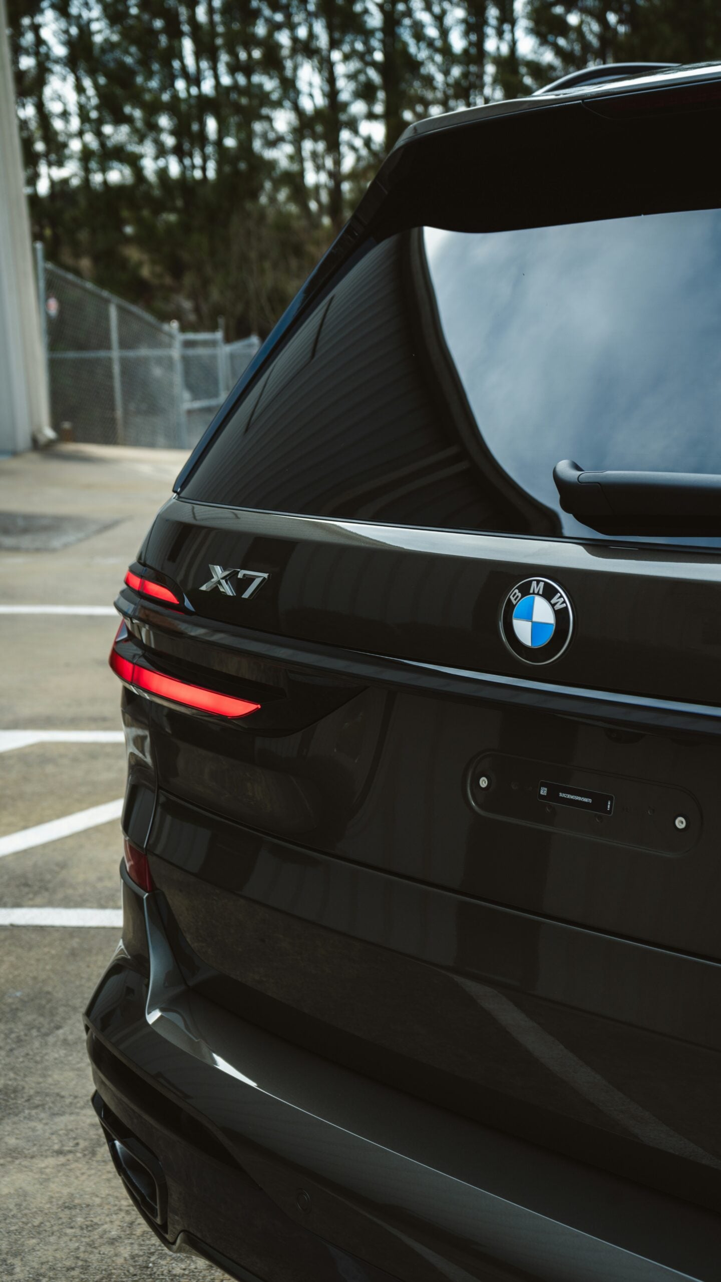 Close-up rear view of a black BMW X7 luxury SUV, showing the X7 badge, BMW emblem, illuminated red taillights, tinted rear window and glossy black bodywork.
