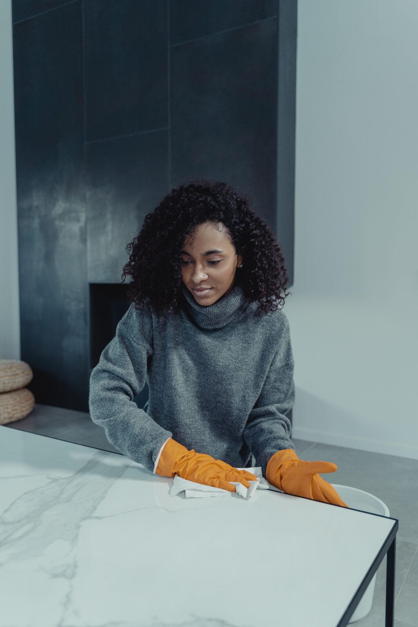 Woman wearing orange rubber gloves wiping a marble-patterned table with a cleaning cloth.
