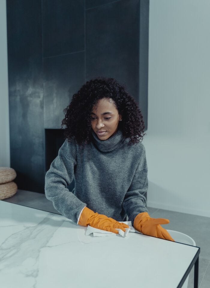 Woman wearing orange rubber gloves wiping a marble-patterned table with a cleaning cloth.