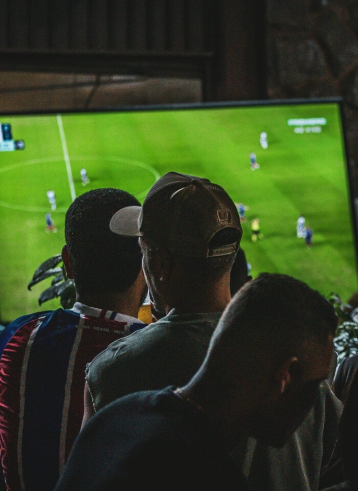 Football fans gathered in a dimly lit bar watching a match on a large television screen.
