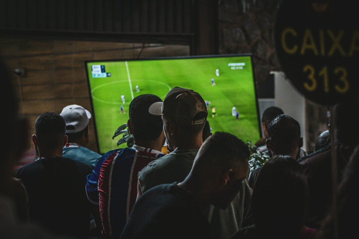Football fans gathered in a dimly lit bar watching a match on a large television screen.