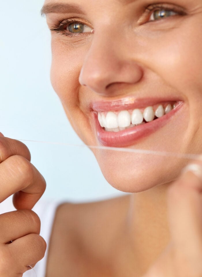 Close-up of a smiling woman with healthy white teeth using dental floss as part of her daily oral hygiene and dental care routine.