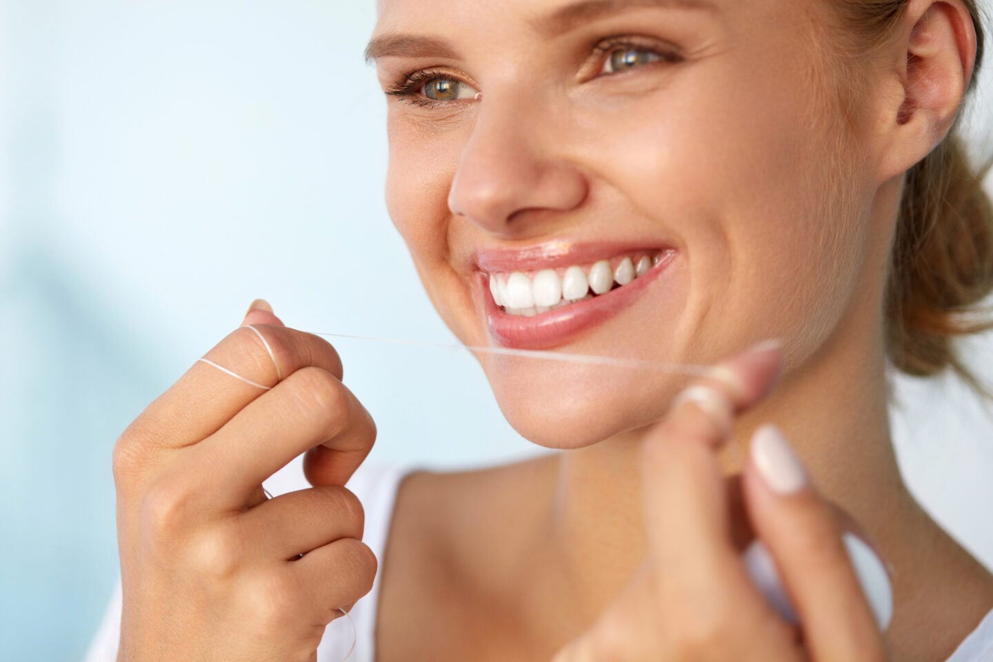 Close-up of a smiling woman with healthy white teeth using dental floss as part of her daily oral hygiene and dental care routine.
