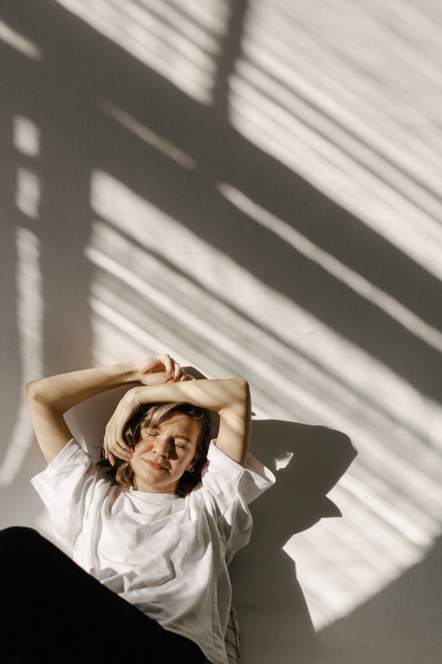 Woman relaxing with her eyes closed and arms raised above her head, enjoying a peaceful moment in natural sunlight.
