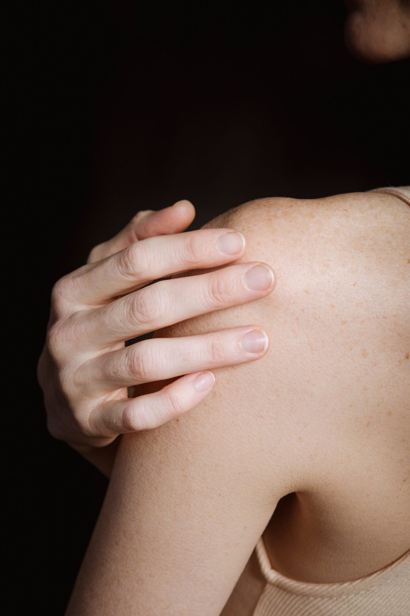 Close-up of a person holding their shoulder with one hand.