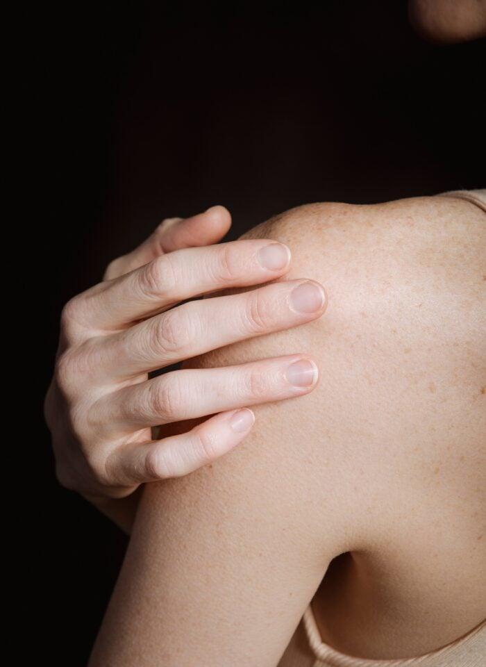 Close-up of a person holding their shoulder with one hand.