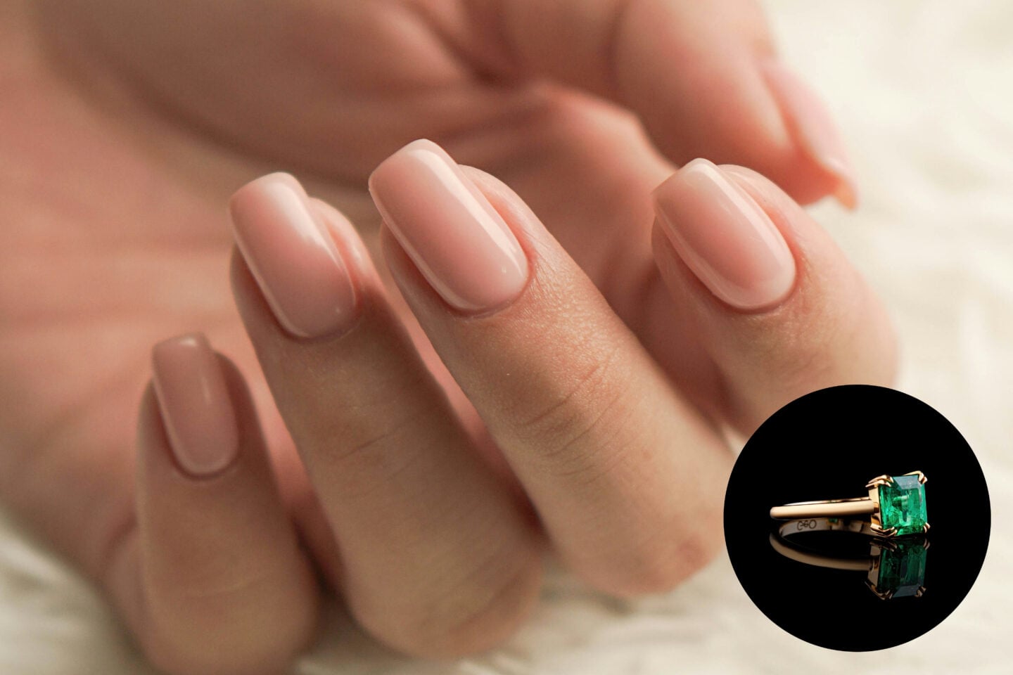 Close-up of a hand with short-to-medium-length, softly squared nails painted in a glossy, pale nude pink shade. A circular inset in the bottom right shows a yellow gold ring featuring a rectangular emerald-green gemstone held in place by four gold prongs against a black background.